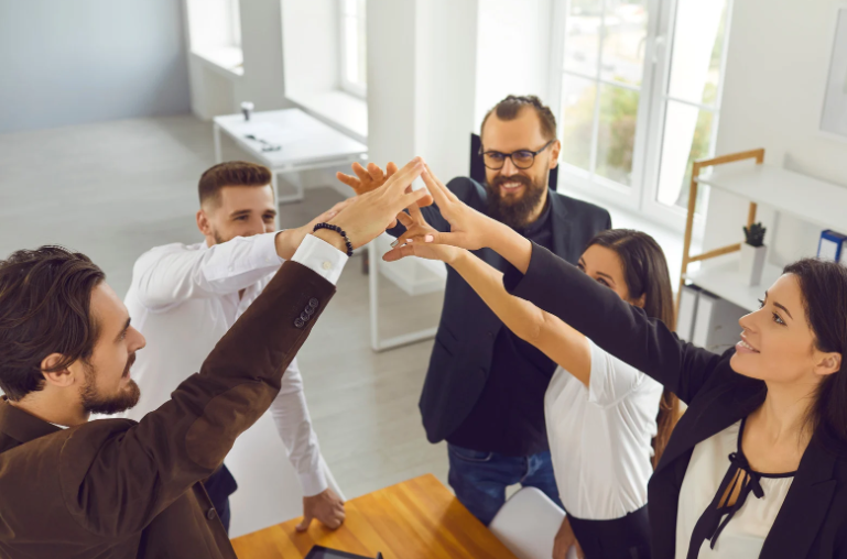 Grupo de cinco personas uniendo sus manos en el centro en señal de trabajo en equipo, con expresiones felices y motivadas. Grupo de cinco personas uniendo sus manos en el centro en señal de trabajo en equipo, con expresiones felices y motivadas.